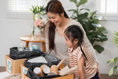 Bir anne kızına evde çeşitli materyalleri sıralayarak geri dönüşümün önemini öğretir. Çevre dostu uygulamalarla uğraşırken aynı gülümsemeyi paylaşıyorlar..