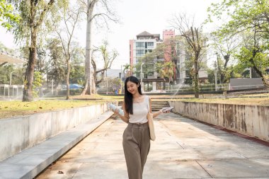 Bir kadın güvenli bir şekilde dışarı çıkar, elinde yeniden kullanılabilir malzemelerle sürdürülebilirliğe olan bağlılığını gösterir, canlı bir kentsel çevre ile çevrilidir..