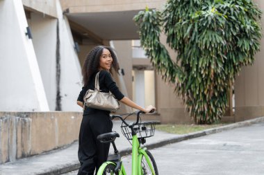 Gülümseyerek arkasını dönen kadın, çevre dostu seyahatini sergiliyor, bir şehir ortamındaki sağlık ve tarz karışımını özetliyor..