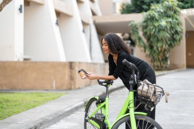 Telefonunu kontrol etmek için ara veren genç bir kadın yoğun gününün tadını çıkarırken çevreci banliyö yaşam tarzını somutlaştırıyor..