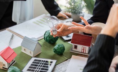 Bir ekip, işbirlikçi bir oturum sırasında sürdürülebilirliği vurgulayan çevre dostu ev modellerini vurgulayarak yenilikçi enerji çözümlerini tartışıyor..