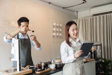 Kalabalık bir kafede, bir barista hassas ölçümler kullanarak kahveyi ustalıkla hazırlarken, bir meslektaşı da kusursuz düzen yönetimi için tablet kullanır..