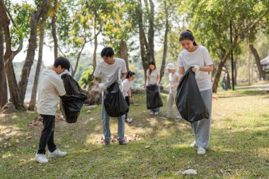 Park temizliğine katılanlar çöp topluyorlar, takım çalışması ve çevresel sürdürülebilirliğe bağlılıklarını gösteriyorlar.