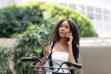 Bir kadın açık hava ortamında telefonda derin düşüncelere dalmışken derin bir nefes almak için durup kahvesini yudumluyor..