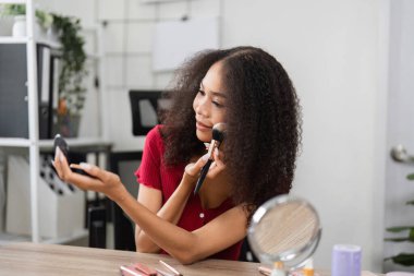 Zarif bir gülümseme ile, bir kadın makyajını düzeltir, doğal güzelliğini kucaklayarak, canlı bir ev ortamında kendini uygulama sürecinin tadını çıkarır..