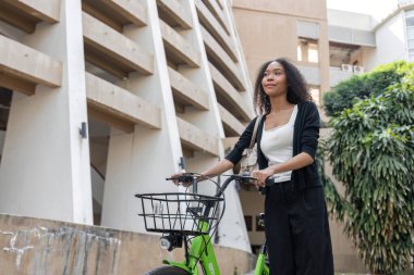 Bir kadın güvenli bir şekilde bisikletinin yanında duruyor, açık havanın tadını çıkarırken sürdürülebilir ulaşım seçeneklerini sembolize ediyor..