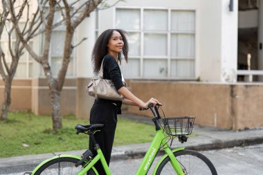 Kendine güvenen genç bir kadın yeşil bisikletiyle poz veriyor, şehri keşfetmeye ve aktif, çevre dostu bir yaşam tarzını benimsemeye hazır..