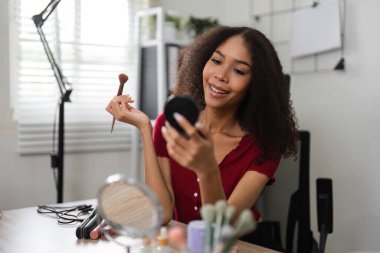 Bir kadın düşünceli bir şekilde makyajını iyi düzenlenmiş yerinde yapar, cilt pozitifliğini somutlaştırır ve eşsiz güzelliğini bir gülümsemeyle kucaklar..