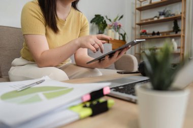 Genç bir kadın, en son teknolojiyle en samimi ofisindeki geleneksel belgeleri dengelemek için tablet üzerindeki çalışmalarını gözden geçiriyor..