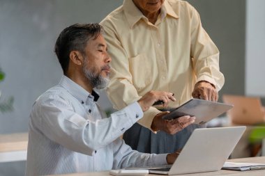 Yaşlı bir beyefendi, modern iş uygulamalarında teknolojinin önemini vurgulayan bir tableti iş danışmanıyla paylaşıyor..