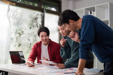 Çeşitli bir ekip, renk örnekleri ve tasarım planlarıyla çevrili UIUX projeleri hakkında detaylı tartışmalara girişerek, bir yenilik ruhunu teşvik eder..