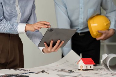 İki inşaat işçisi çalışma alanlarında ortak bir tartışmaya girişerek, proje iş akışlarını geliştirmek ve etkili iletişimi sağlamak için dijital araçlardan yararlanıyor.