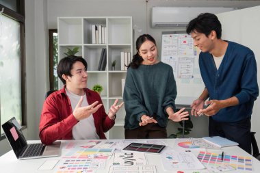 Tasarım malzemeleri ve konseptlerle dolu bir masanın etrafında bir grup profesyonel beyin fırtınası yaparak projelerini geliştirmek için dinamik tartışmalara giriştiler..