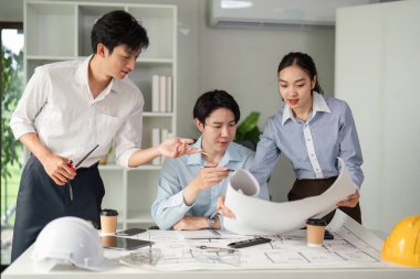 Bir grup genç profesyonel, dinamik bir ofis ortamında mimari planlar, fikirler ve içgörüler üzerinde işbirliği yapıyor..