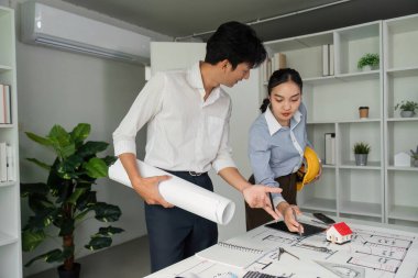 Ekip üyeleri mimari planlar ve proje için ortak vizyonlarını sergileyen bir model üzerinde strateji oluştururken ayrıntılı bir tartışma ortaya çıkıyor..