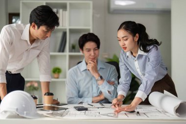 Profesyoneller masa etrafında bir tartışmaya giriştiler, mimari planları değerlendirdiler ve bir proje için yeni fikirler öne sürdüler.