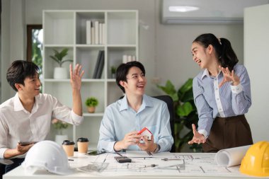 Etkileşimli bir ortamda ekip, yaratıcılıklarını ve takım çalışmalarını vurgulayarak bir mimari projeyi tartışırken kahkahaları paylaşıyor. Model ev konuşmalarının merkezidir..