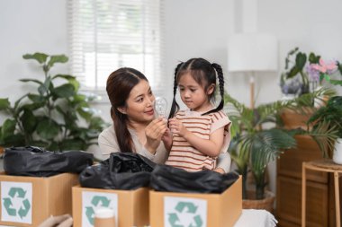 Şefkatli bir anne, kızına geri dönüşümün önemini anlatan bir ampul gösterir. Evdeki materyalleri sınıflandırırlar ve çevresel farkındalığı artırırlar..