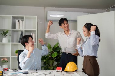 Üç profesyonelden oluşan bir ekip proje planlarını tartışırken ve çalışma alanlarında coşku gösterirken heyecan verici bir işbirliği anını paylaşıyor..