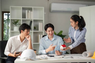 Takım üyeleri mimari tasarımlar hakkında üretken bir tartışmaya girişerek fikirlerini görselleştirmek için bir model kullanıyorlar. Ortak çabaları takım çalışmasını ve yenilikleri vurguluyor.