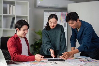 Bir grup tasarımcı renk seçimleri ve modellemeleri analiz ederken beyin fırtınaları yapıyor ve görsel olarak uyarıcı bir ortamda takım çalışmalarını ve yaratıcılıklarını gösteriyor..