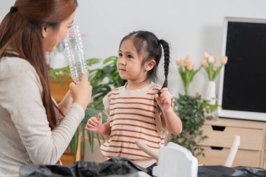 Bir anne plastik şişelerin nasıl geri dönüştürüldüğünü gösterirken, kızı ilginç bir şekilde gözlemliyor, çevre dostu uygulamalara karşı bir sevgi besliyor..