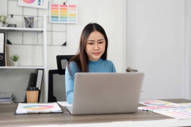 Masasında oturan tasarımcı, düşünceli bir şekilde kahve içerken ve yeni fikirler geliştirirken dizüstü bilgisayarına odaklanıyor..