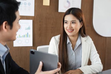 İki profesyonel, çağdaş bir ofis alanında yapılan ortak bir toplantıda tablet üzerindeki çizelge ve stratejileri analiz ederek önemli iş konularını tartışıyor..