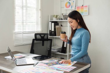 Bir tasarımcı renk seçeneklerini değerlendirirken kahvesinden zevk alır, yaratıcı ve üretken bir karar verme anını şık bir çalışma alanında yansıtır.