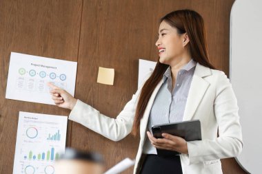 Seyircilerinin dikkatini çeken bir kadın, proje yönetim çizelgelerine işaret ediyor. Uzmanlığını sergilediği sırada ilgi çekici bir sunum yapıyor..