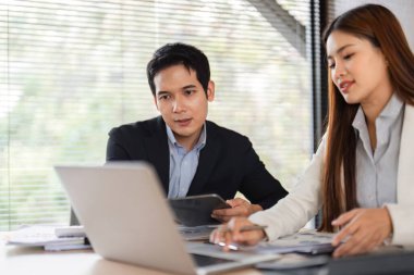 Bir erkek dikkatle izler, bir kadın bilgiyi laptopta analiz ederken, modern bir iş ortamında takım çalışması sergilerken..