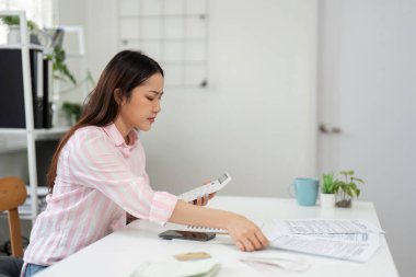 Huzurlu ev ofisinde çalışan bir kadın, iş malzemelerini ustalıkla sınıflandırarak, iş akışındaki yaratıcılığı ve organizasyonu vurgular..