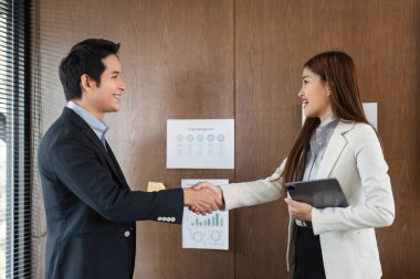 Parlak bir ofiste, bir erkek ve bir kadın, karşılıklı saygı ve ortak hedefler üzerine kurulmuş güçlü bir mesleki ilişkiyi yansıtan el sıkışırlar..