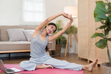 Rahat bir ifadeyle, bir kadın yoga minderinin kenarına eğilir, esnekliğini ve sükunetini benimser ve şık yaşam alanında....