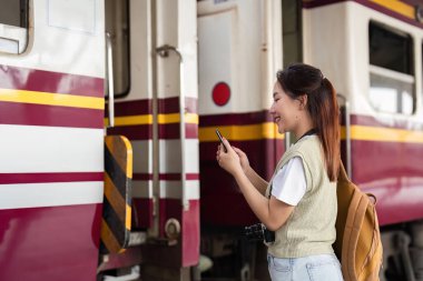Neşeli bir gezgin tren istasyonunda duruyor. Yolculuğuna hazırlanırken telefonunu heyecan verici bir şekilde kontrol ediyor..
