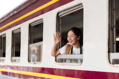 Gülümseyen bir gezgin, önündeki yolculuk ve karşılaşacağı maceralar hakkında sevinç ve heyecanı ifade eden bir tren penceresinden el sallar..
