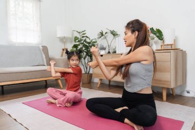 Bir anne ve kızı, evdeki yoga minderinin üzerinde esneyerek, iletişim kurarak ve refahı destekleyerek neşeli bir anı paylaşıyorlar..