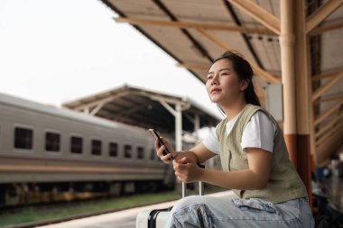 Düşünceli bir gezgin, tren istasyonunda akıllı telefonunu kullanarak yolculuk hazırlığının özünü yakalar..