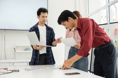 Bir işbirliği oturumu sırasında, bir ekip üyesi iş arkadaşlarıyla birlikte renk örneklerini değerlendirir, etkili tasarım için teknoloji ve yaratıcılığı birleştirir..