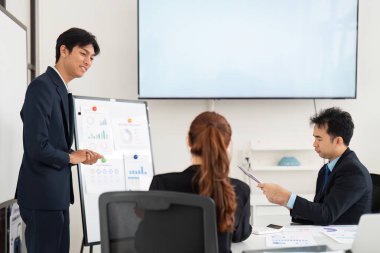 Yönetim kurulu sunumunda genç profesyonel takım üyeleriyle görüşerek, stratejik tartışmalar için işbirlikçi bir ortam oluşturarak veri analizini açıklıyor..