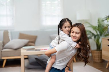 Okula gitmeden önce, bir annenin kızını sırtında taşıdığı sıcak bir an paylaşılır. Beraberliğin sevincini vurgular..