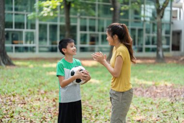 Gülümseme paylaşımı, genç bir çocuk dışarıda antrenman yaparken bir kadınla strateji tartışırken bir futbol topu tutuyor..