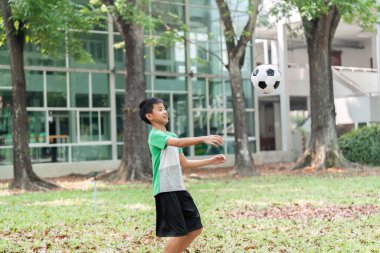 Yeteneklerini geliştirmeye odaklanan bir çocuk, yeşil bir parkta futbol yakalama tekniğini geliştiriyor ve doğal ortamın tadını çıkarıyor..
