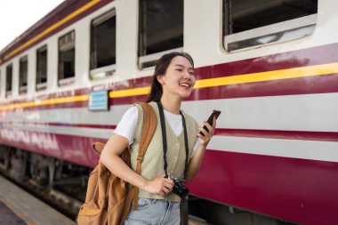 Işıldayan mutluluk, genç bir gezgin trenin yanında duruyor, akıllı telefonuyla bağlantının tadını çıkarırken bir sonraki yolculuğunu tahmin ediyor..