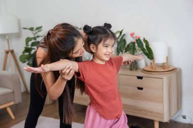 Bir anne, kızına destek olurken birlikte esneme egzersizleri yapar, hareketlerini teşvik eder ve neşeli bir ev ortamında iletişim kurar..