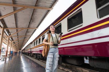 Bir gezgin heyecanlı bir tren istasyonunda heyecanla trenini bekliyor, maceraya hazır. Telefonunu gülümseyerek kontrol ediyor. Keşif ruhunu somutlaştırıyor..
