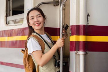 Neşeli bir şekilde gülümseyen genç bir kadın, yeni maceraları ve seyahatin heyecanını simgeleyen bir trene biner..