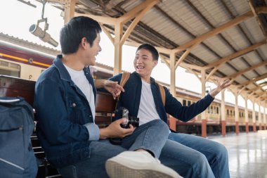 İki genç gezgin tren istasyonunda oturup bir sonraki maceralarını sabırsızlıkla beklerken öykülerini ve kahkahalarını paylaşıyorlar..