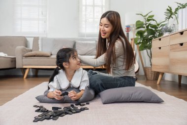 Mutlu bir anne yerde domino taşlarıyla oynarken kızlarının saçlarını tarar. Bu eğlenceli etkileşim aile bağlarını ve neşeli anları vurguluyor..