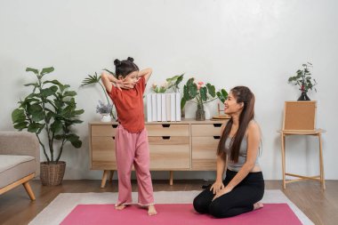 Bir anne, kızı yoga sürecini gösterirken neşe ve destek veriyor. Vücut geliştirme yoluyla kalpten bağlarını vurguluyor..